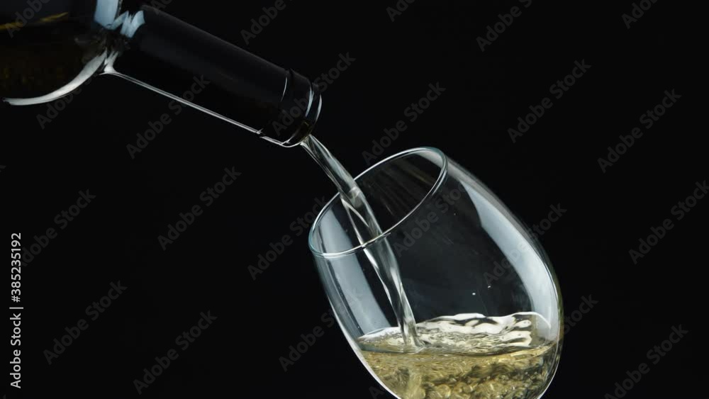 White wine. Pouring white wine from the bottle into a wineglass. Wine in glass on black background.