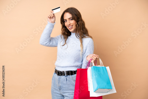 Young woman over isolated background holding shopping bags and a credit card