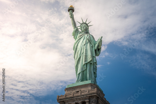 Shot of the Statue of Liberty in New York City  Usa. The shot is taken during a beautiful sunny day with a blue sky and white clouds in the background