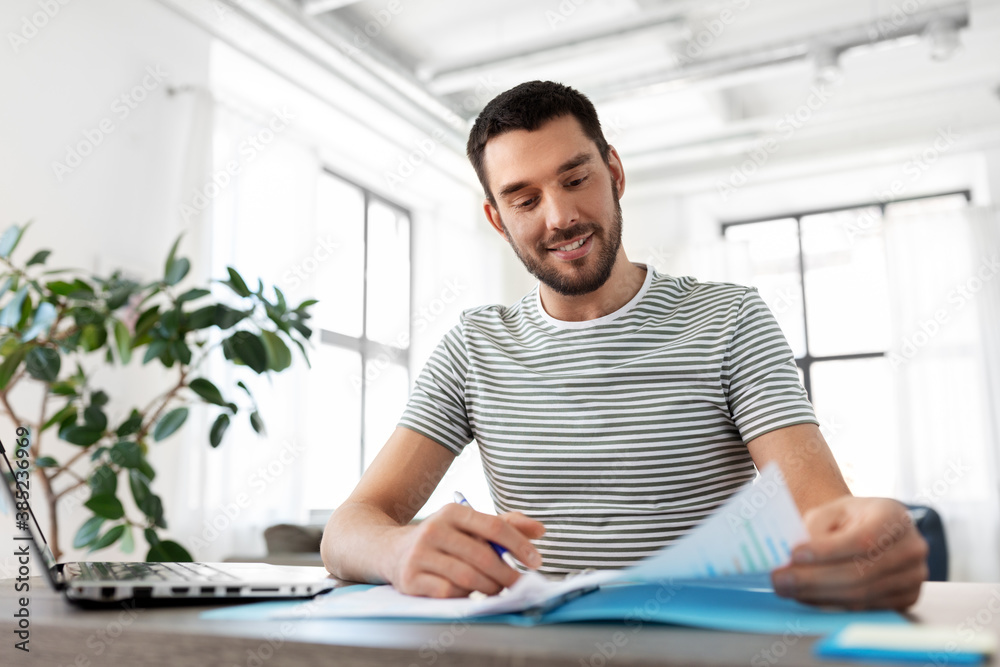 remote job and business concept - happy smiling man with papers and laptop computer working at home office