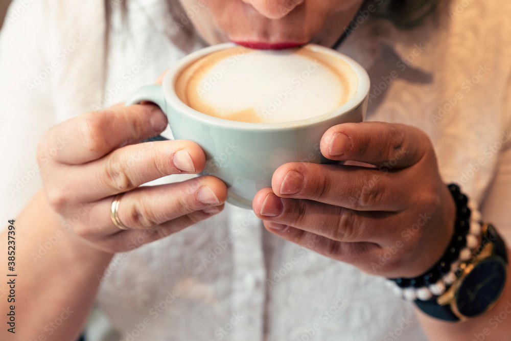 Woman holding and drinking a cup of coffee with heart. Hands and hot mug of cappuccino. Close up. Woman holding and drinking a cup of coffee with heart. Hands and hot mug of cappuccino. Close up.