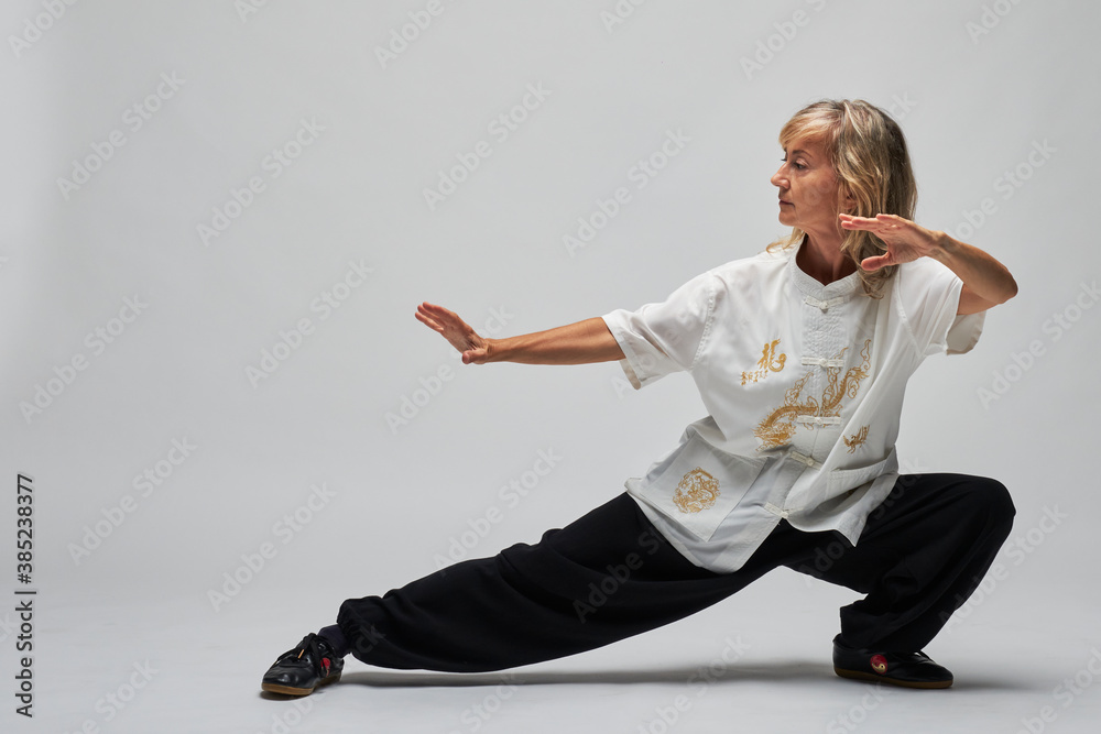 Mature blonde woman practicing Chi kung and Chi on white background. She wears a traditional white chinese Tai Chi jacket, black trousers and shoes with ying symbol Stock