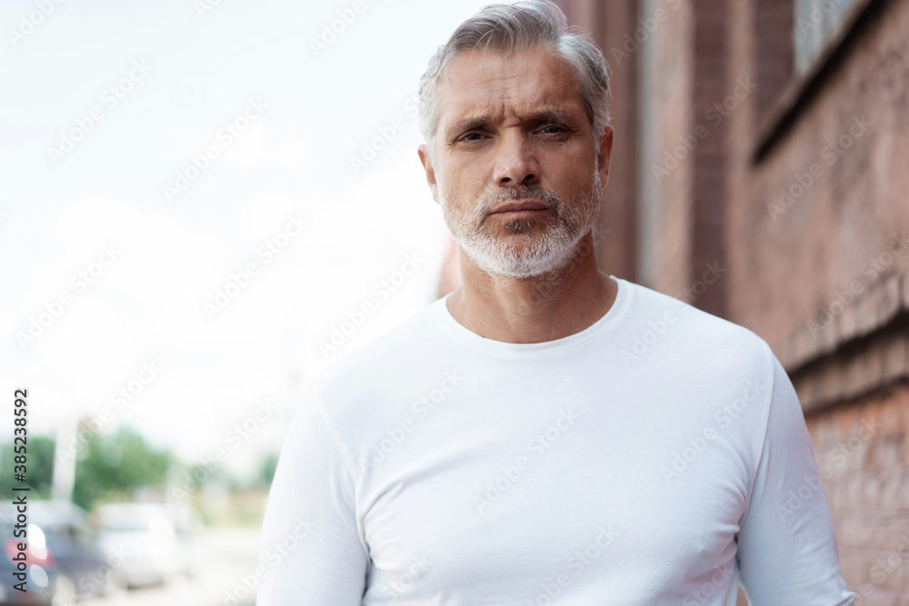 Portrait of a Grey-haired Mature handsome man in jeans and white t-shirt leaning to the old wall. Portrait of a Grey-haired Mature handsome man in jeans and white t-shirt leaning to the old wall.
