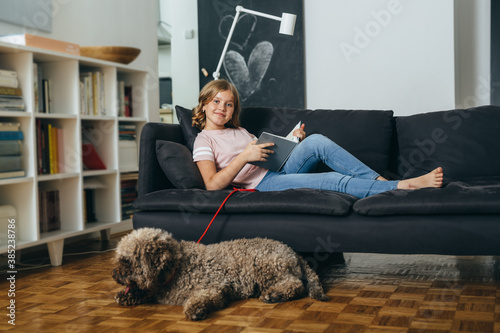 teenager girl sitting on sofa with her dog at home and reading book