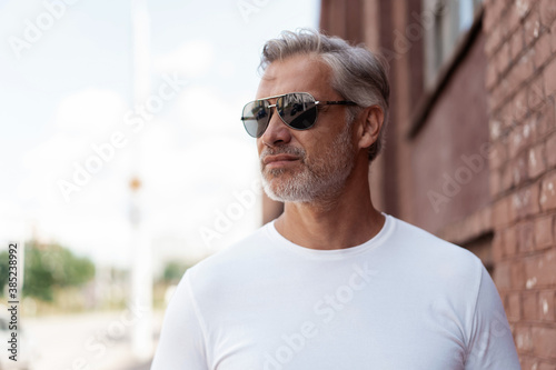 Portrait of a Grey-haired Mature handsome man in jeans and white t-shirt leaning to the old wall.