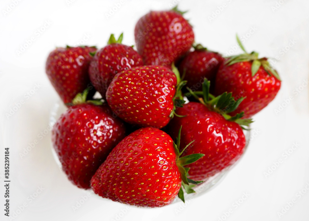 large red strawberries in a glass plate on a white background top view. red fruit is close large red strawberries in a glass plate on a white background top view. red fruit is close