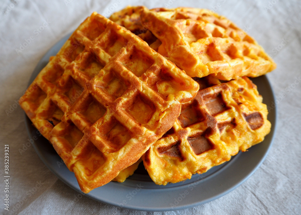 four fresh Belgian waffles made from cornmeal, eggs and pumpkin lie on a grey round plate on a beige tablecloth side view . gluten-free homemade food four fresh Belgian waffles made from cornmeal, eggs and pumpkin lie on a grey round plate on a beige tablecloth side view . gluten-free homemade food