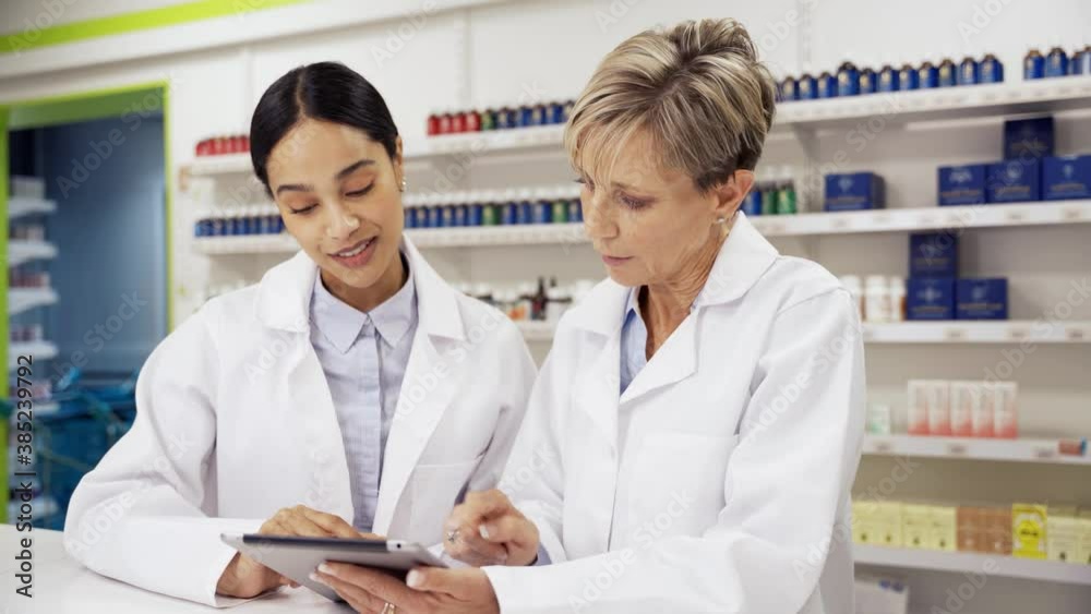 Female intern being assisted by caucasian pharmacist locating pills in pharmacy Female intern being assisted by caucasian pharmacist locating pills in pharmacy