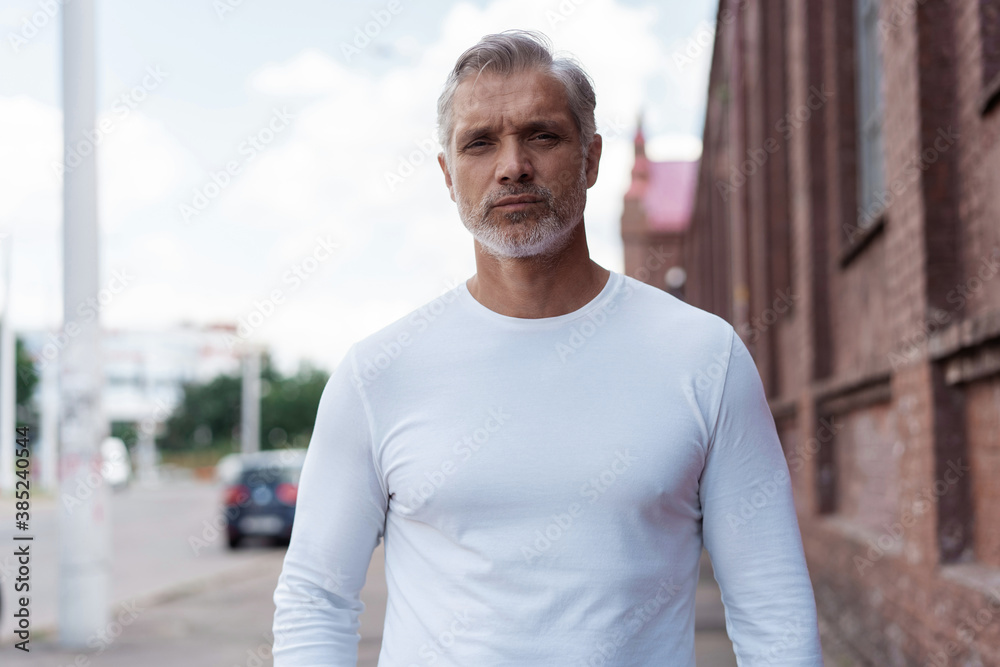 Portrait of a Grey-haired Mature handsome man in jeans and white t-shirt leaning to the old wall. Portrait of a Grey-haired Mature handsome man in jeans and white t-shirt leaning to the old wall.