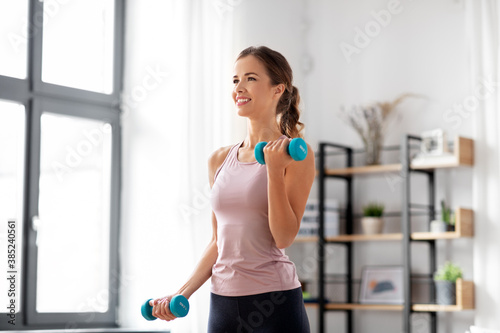 fitness, sport and healthy lifestyle concept - smiling young woman with dumbbells exercising at home