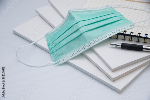 Medical mask, notebook with pen and book on white
