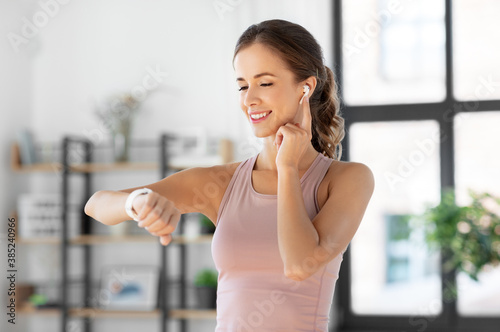 sport, fitness and technology concept - happy smiling young woman with smart watch and earphones exercising at home Free Download sport, fitness and technology concept - happy smiling young woman with smart watch and earphones exercising at home - GFXLoad