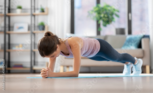 fitness, sport, training and people concept - young woman doing plank exercise on mat at home