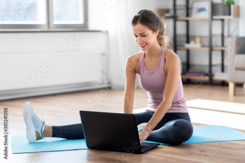 fitness, technology and healthy lifestyle concept - woman with laptop computer doing sports at home