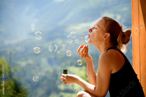 A girl in a calm mood blows bubbles overlooking the mountain landscape.