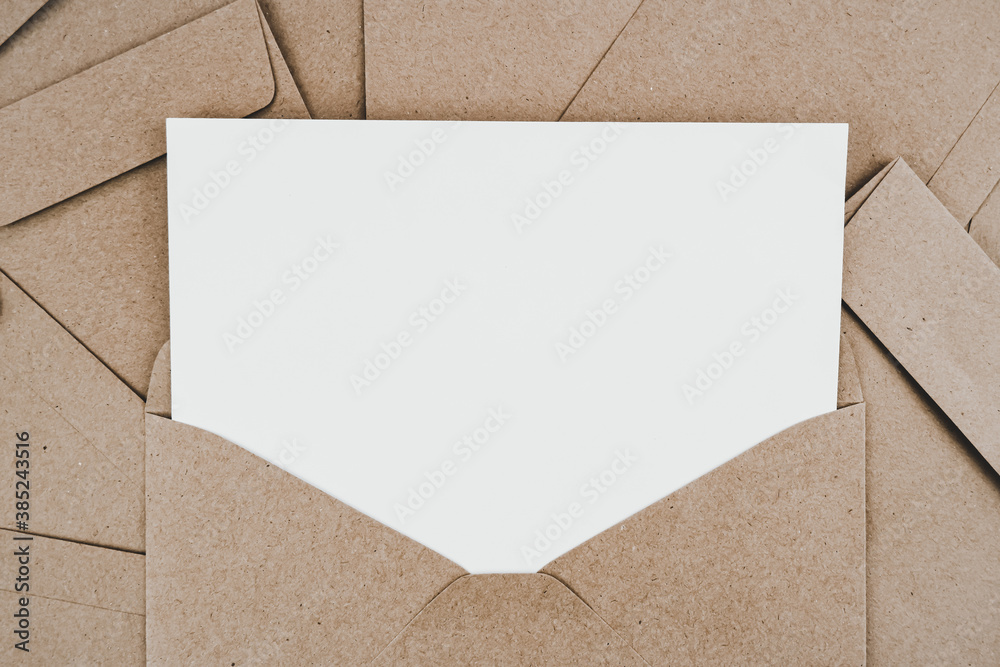 Blank white paper is placed on the open brown paper envelope. Mock-up of horizontal blank greeting card. Top view of Craft paper envelope on white background. Flat lay of stationery. Minimalism style. - obrazy, fototapety, plakaty 