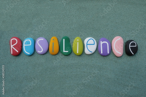 Resilience, the ability to be happy or successful again after something difficult or bad has happened. Creative handmade multicolored stone letters of resilience text over green sand