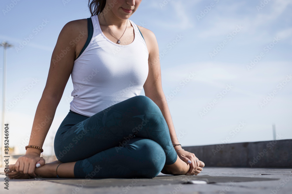 Sporty young woman doing Yoga exercises using a gym mat along the beach in Lisbon, Portugal. Playful woman working as freelance Yoga teacher doing fitness workout on the beach at sunset. Healthy life