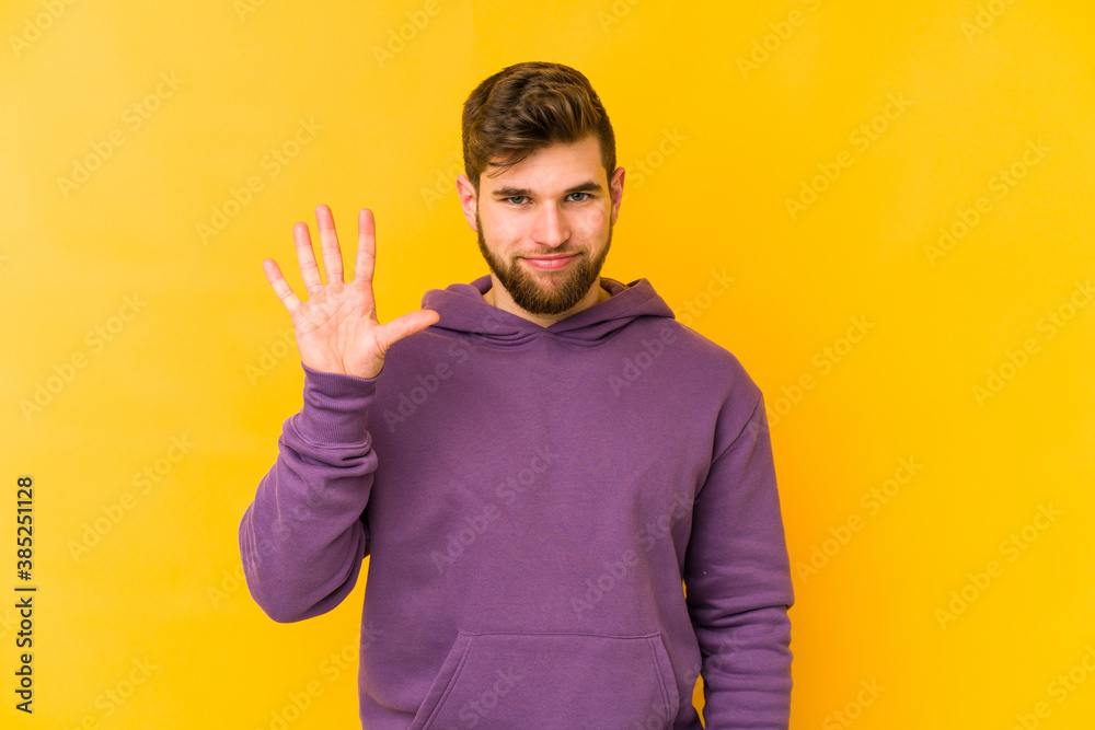 Young caucasian man isolated on yellow background smiling cheerful showing number five with fingers. Young caucasian man isolated on yellow background smiling cheerful showing number five with fingers.