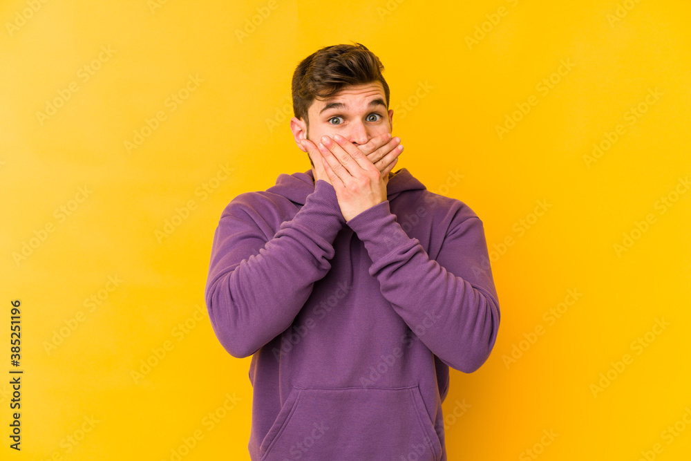 Young caucasian man isolated on yellow background covering mouth with hands looking worried.