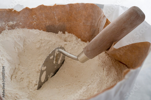 Close-up of plaster trowel in full open paper bag of putty powder for wall decoration,caulk or glaze.Concept of building materials.Finish coating in dry cement powder form.Selective focus,copy space.