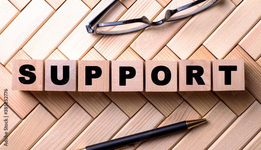 The word SUPPORT is written on wooden cubes on a wooden background next to a pen and glasses. The word SUPPORT is written on wooden cubes on a wooden background next to a pen and glasses.