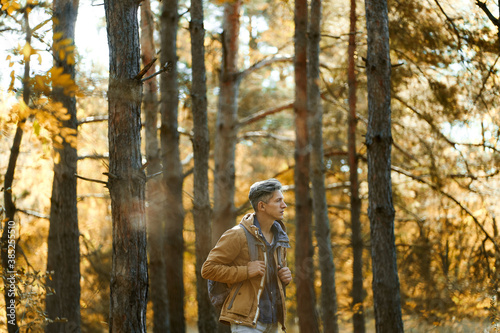 casual style man in autumn woods with backpack, single hiking in depths of a forest