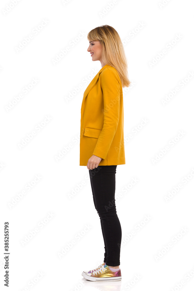 Side View Of Young Woman In Yellow Jacket, Black Jeans And Colorful Sneakers. Side View Of Young Woman In Yellow Jacket, Black Jeans And Colorful Sneakers.
