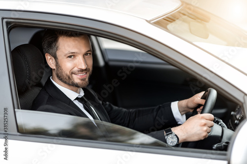 Cheerful successful businessman looking through car window