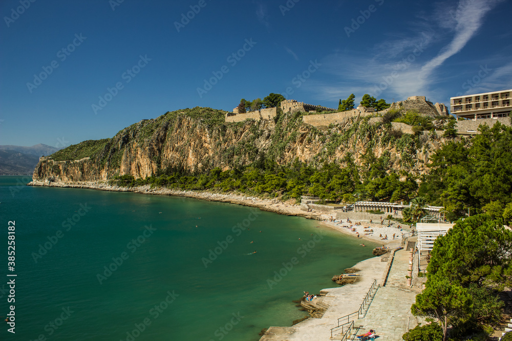 Greece sea bay shore line summer vacation season scenic view with rocks and ancient castle ruins on top clear weather day time and people on beach