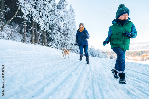 Mother and son having a fun. They running with their beagle dog in snowy forest during dog walk. Mother and son relatives and femily values concept image.
