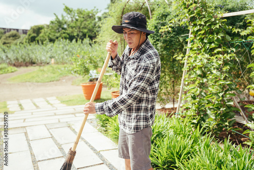 Asian senior farmer cleaning garden with a broom stick in a farm.