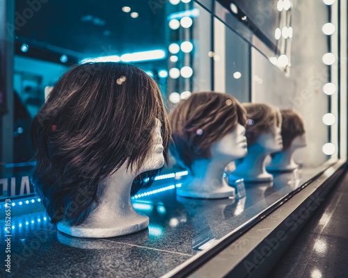 White foam female mannequins heads in a row on a store window at night. Blue and white neon lights and glare on glass. Nightlife of the metropolis.