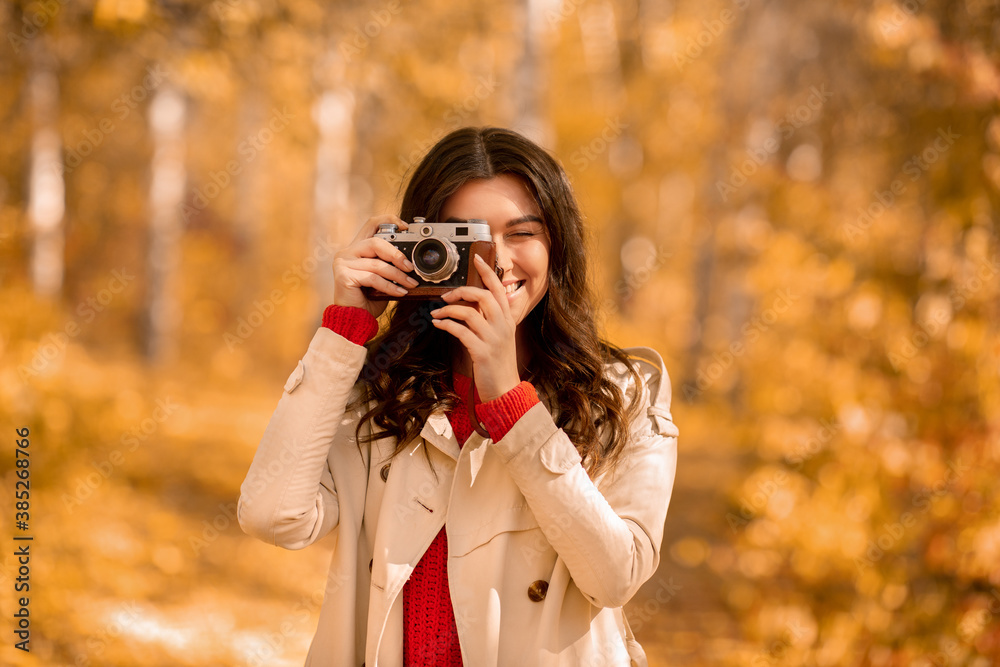Portrait of happy female photographer with retro camera taking pictures of beautiful autumn at park