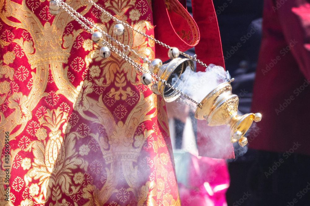 A smoking censer in the hand of an Orthodox Christian priest in an embroidered church cassock.