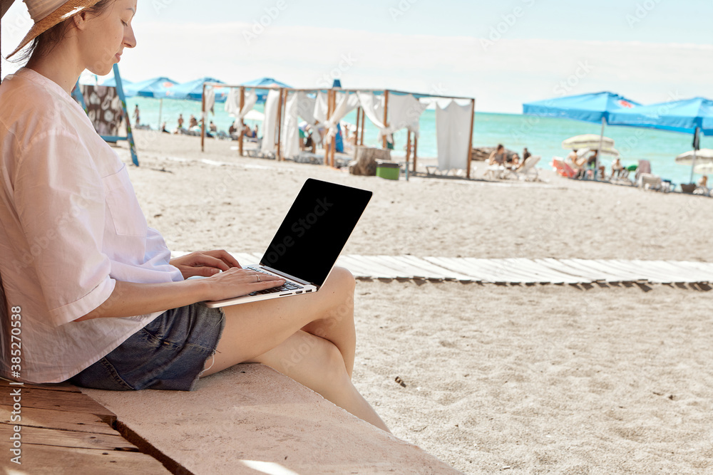 Young woman using laptop computer on a beach. Freelance work concept..Pretty young woman using laptop in cafe on tropical beach in outdoor cafe terrace with sea view. Work and travel