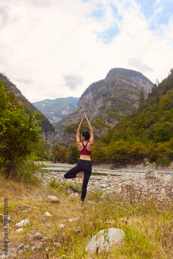 Yoga classes in nature. A woman does yoga in the mountains, near a mountain river flows. The concept of playing sports alone. Social exclusion Yoga classes in nature. A woman does yoga in the mountains, near a mountain river flows. The concept of playing sports alone. Social exclusion