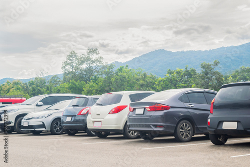 Car parked in large asphalt parking lot with trees, cloudy sky and mountain background. Outdoor parking lot with fresh ozone and green environment of travel transportation concept © merrymuuu