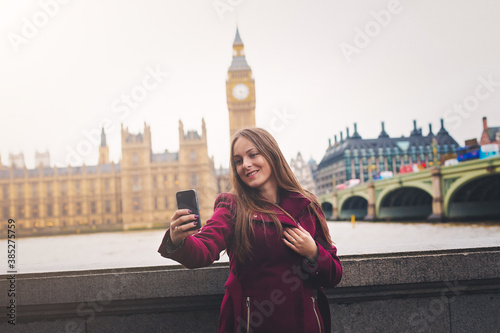 Young London traveller woman takes selfie pictures with her phone at Westminster with view to the Big Ben Tower in London, UK