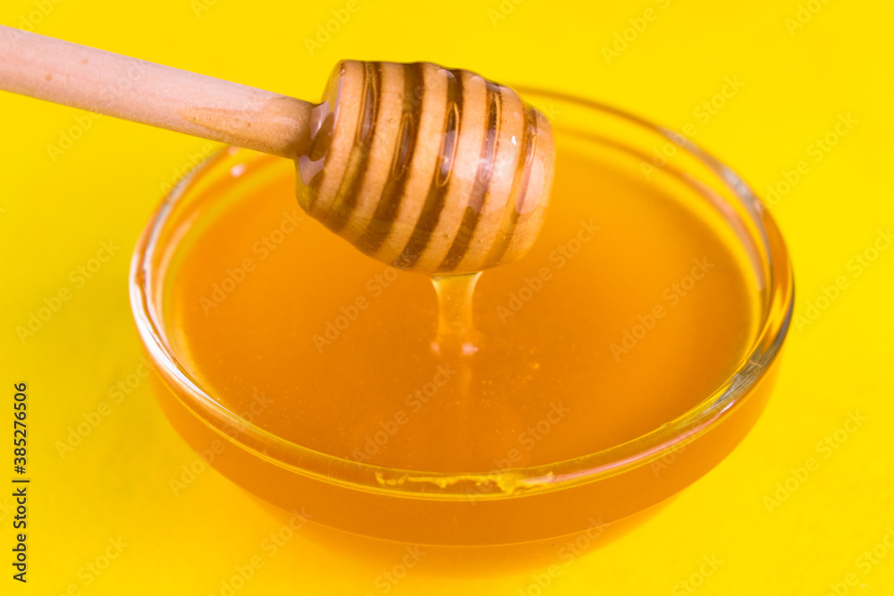 Honey in a glass bowl flows down the honey stick on a yellow background.
Close-up.
Honey in a glass bowl flows down the honey stick on a yellow background.
Close-up.