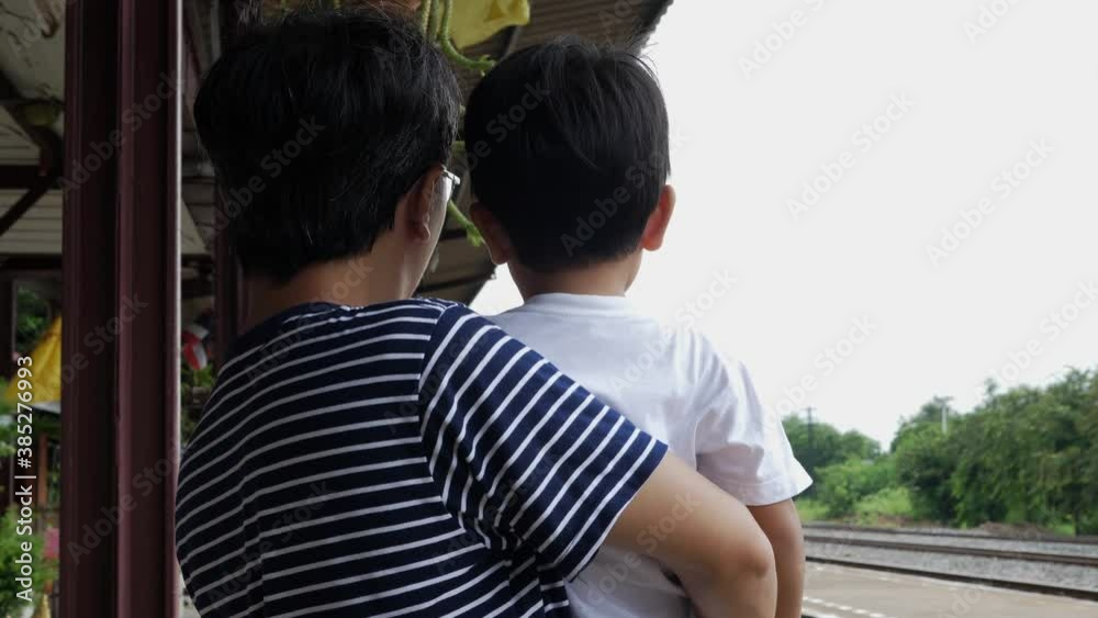 4K Asian father and cute child boy wait to see train at railway station outdoor. Dad carrying son travel outdoor. Happy family activity and learning concept. Train coming in the end. 4K Asian father and cute child boy wait to see train at railway station outdoor. Dad carrying son travel outdoor. Happy family activity and learning concept. Train coming in the end.