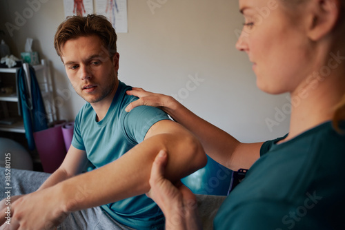 Young man undergoing physiotherapy treatment for hand injury with woman doctor