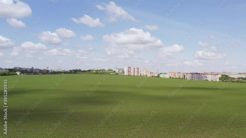 Moving across a green field approaching a cluster of high-rise apartment or office blocks at the edge of a town under a cloudy sunny blue sky Moving across a green field approaching a cluster of high-rise apartment or office blocks at the edge of a town under a cloudy sunny blue sky