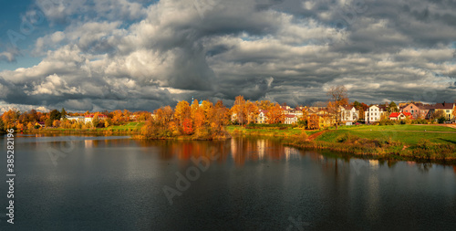 Wide panorama of the dramatic countryside with cottages and yellow trees on the lake shore.
