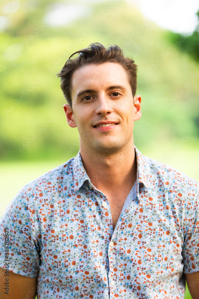Portrait of smiling young caucasian man in green park outdoors.