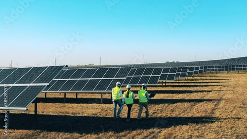 Safety inspectors are walking along the photovoltaic power field at a solar energy power plant.