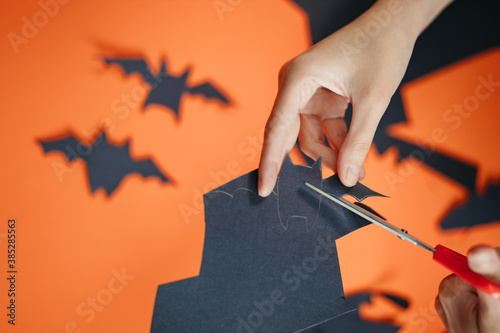 Overhead closeup shot of a woman cutting out bat shapes from black paper. DIY Halloween arts and crafts as home activity for kids. photo