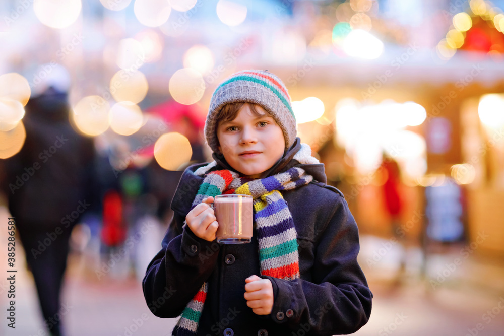 Little cute kid boy drinking hot children punch or chocolate on German Christmas market. Happy child on traditional family market in Germany, Laughing boy in colorful winter clothes