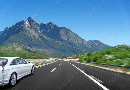 A white car rushes along the road against the backdrop of a beautiful countryside landscape. © Denis Rozhnovsky