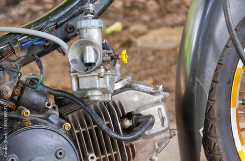 Take a close-up shot of the Motorcycle engine carburetor against the blurry background.